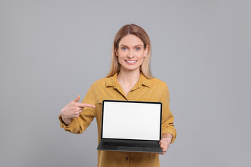 Naklejka premium Happy woman showing laptop on light grey background