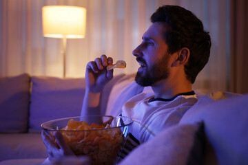 Man eating chips while watching TV on sofa at night. Bad habit