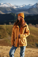 Woman fall stands a smile travels to the mountains in nature on a hike and happiness in a yellow raincoat against the snowy mountains in the sunset, freedom of life style
