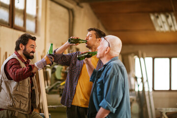 Small group of carpenters enjoying a cold bottle of beer after a hard days work in their woodworking workshop