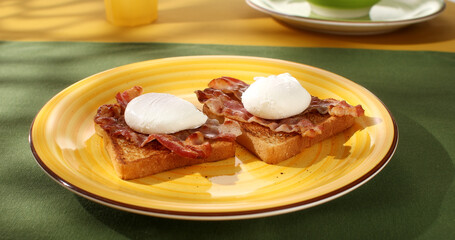 Toast with poached egg and bacon on a plate. Serving breakfast on a colored background. Boiled eggs on bread with fried bacon. Angle view. 