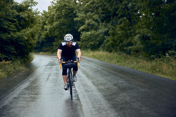 Sportive, young, bearded man, cyclist in helmet, glasses and uniform riding bike on wet road in cloudy chill evening. Concept of sport, hobby, leisure activity, training, health, speed, endurance, ad