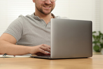 Man working with laptop at wooden table indoors, closeup