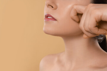 Young woman massaging her face on beige background, closeup. Space for text