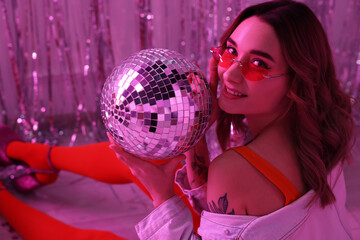 Naklejka premium Beautiful woman in stylish outfit with disco ball at party indoors, toned in pink