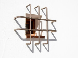 Ventana enrejada a pleno sol en una fachada de una casa blanca y su sombra