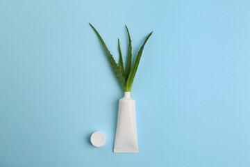 Tube of toothpaste and fresh aloe on light blue background, flat lay