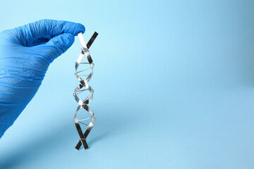 Scientist with DNA molecular chain model made of metal on light blue background, closeup. Space for...