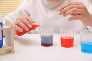 Girl mixing colorful liquids at white table indoors, closeup. Chemical experiment set for kids