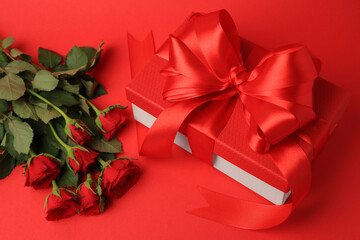 Beautiful gift box with bow and roses on red background