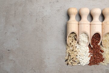 Scoops with different sorts of rice on grey table, flat lay. Space for text