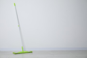 Mop with plastic handle near wall indoors. Space for text