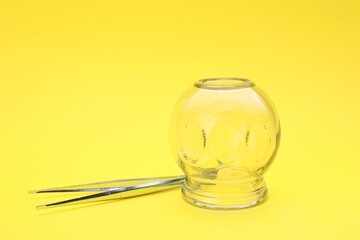 Glass cup and tweezers on yellow background, closeup. Cupping therapy