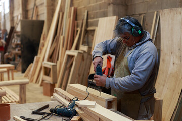 Ageless Skills: Seasoned Artisan Operating a Drill in a Woodworking Studio