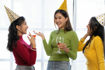 Three beautiful girls wearing party hats are having fun celebrating their birthday in colorful...