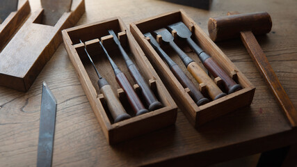 Japanese wood working tools on an old rustic work table. Vintage Japanese block planes, chisels and hammers, in light and shadow. 