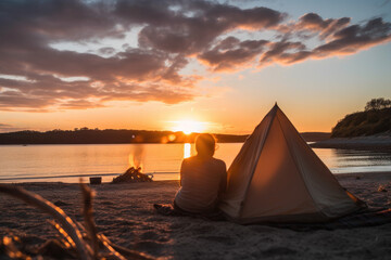 Young couple camping and relaxing on a beach watching the sun set. Silhouettes with setting sun., generative ai