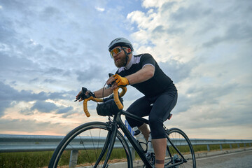 Active lifestyle. Sportive, bearded, young ,a in helmet riding road bike on chill., cloudy evening on empty road. Concept of sport, hobby, leisure activity, training, health, speed and endurance, ad