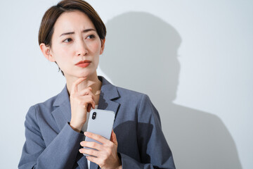 スマートフォンを持ちながら悩んでいる若い女性　ビジネスイメージ