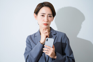 スマートフォンを持ちながら悩んでいる若い女性　ビジネスイメージ