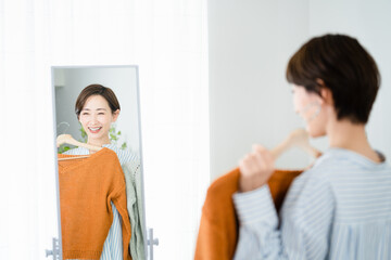 鏡の前で服選びをしている若い女性　ファッションイメージ	