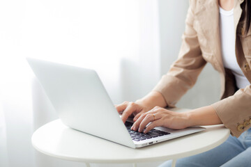 Closeup hands of businesswoman working on laptop computer on desk at home office, freelance looking and typing on notebook on table, lifestyles of woman studying online, business concept.