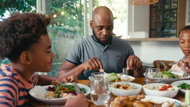 Close up of family sitting around table at home enjoying meal together - shot in slow motion