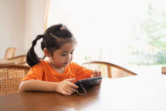 Asian Child Girl Looking Using And Touch Mobile Phone Screen. Baby Smiling Funny Time To Use Mobile Phone. Too Much Screen Time. Cute Girl Watching Videos While Tv, Internet Addiction Concept.