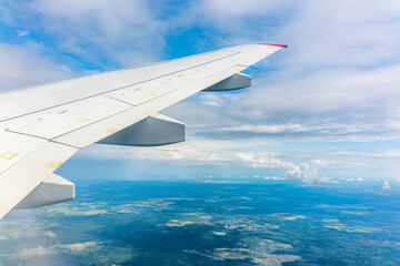 Obraz premium View of airplane wing, blue skies and green land during landing. Airplane window view.