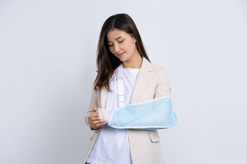 Young beautiful asian businesswoman with broken arm and bandage standing isolated on white...