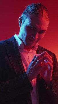 Vertical video. Evil plan. Exciting expectation. Red blue color neon light tricky sly smirking man waiting tenting fingers on dark.