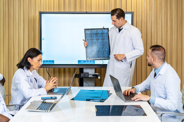 Fototapeta premium Hospital Conference Meeting Room: Male Physician Presents Patient X-ray on TV Screen, Team of Medical Doctors Discuss Treatment. Research Scientists Talk of Cure, Drug, Medicine Development