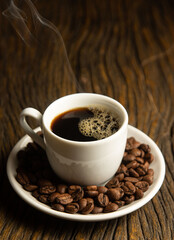 Fototapeta premium hot coffee in white cup with coffee beans on wooden table 