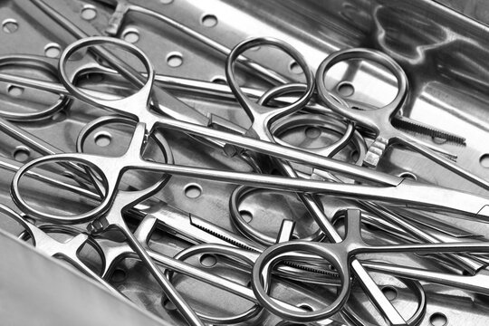 Closeup view stainless surgical needle drivers lying down on steel sterilization tray medical tools