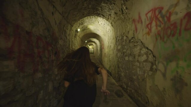 frightened girl with loose hair runs away from a stranger through a gloomy tunnel