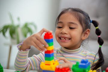 Adorable little girl playing toy blocks in a bright room.