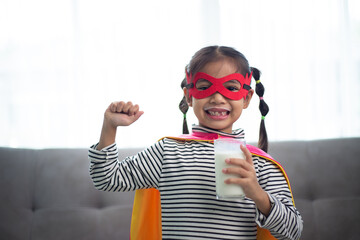 Asian little girl in a superhero costume drinking milk at home. Healthy Concept.
