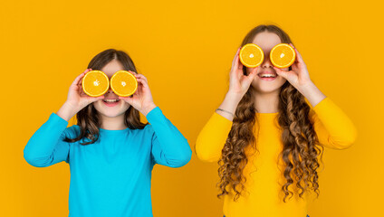 funny teen girls hold orange fruit on yellow background
