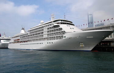 Silver luxury cruiseship cruise ship liner Whisper or Shadow at Ocean Cruise Terminal in Kowloon with view of Hong Kong, Hongkong skyline during Asia cruising