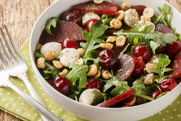 Homemade arugula salad, baked beets, ripe cherries, mozzarella, hazelnuts close-up in a bowl on the table. Horizontal