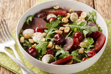 Vegetarian salad of arugula, beets, ripe cherries, cheese, hazelnuts close-up in a bowl on the table. Horizontal