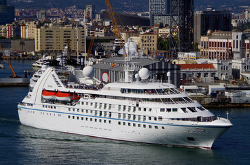 Luxury Wind Star cruiseship cruise ship liner yacht Breeze departure sail away from port of Barcelona, Spain with marina and city skyline in background and other maritime vessels yachts