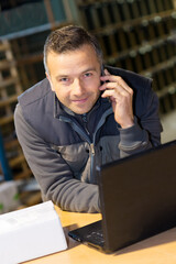 portrait of smiling storeman with laptop and using cellphone - obrazy, fototapety, plakaty