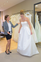 Naklejka premium female trying on wedding-dress with women assistant