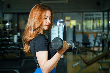 Asian young female workout with dumbbell weight training at fitness center.