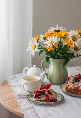 Summer tea party - a cup of green tea, a piece of berry pie, a jug with garden flowers on a round table in the living room