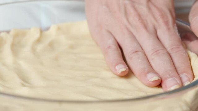 A woman uses her hands to evenly spread the dough in a glass baking dish.