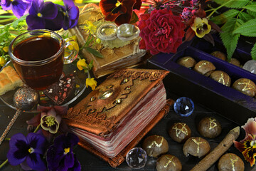 Still life with flowers, magic book of spells, cups on witch ritual table. Occult, esoteric and...