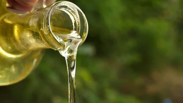 slow motion shot of extra virgin olive oil being poured from a clear glass bottle