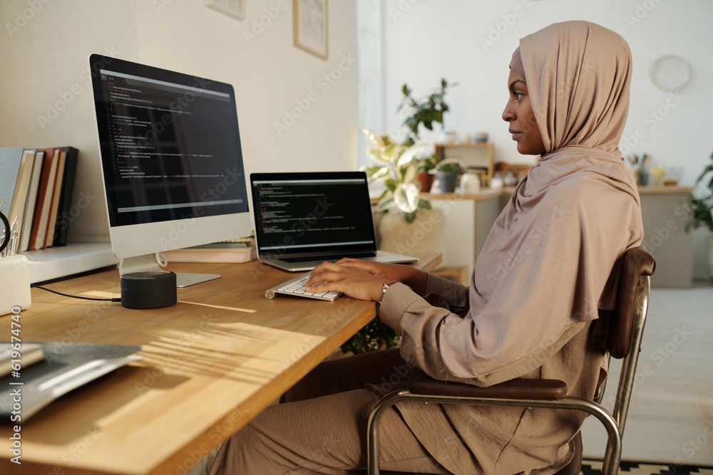 Aufkleber Young creative female webdesigner typing on computer keyboard and looking at screen with data while creating new website or software
